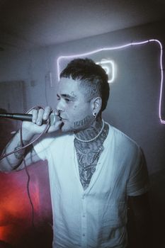 A tattooed man passionately singing into a microphone at a lively indoor party.