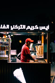 Ice cream vendor at night in a bustling urban environment, serving from a booth.