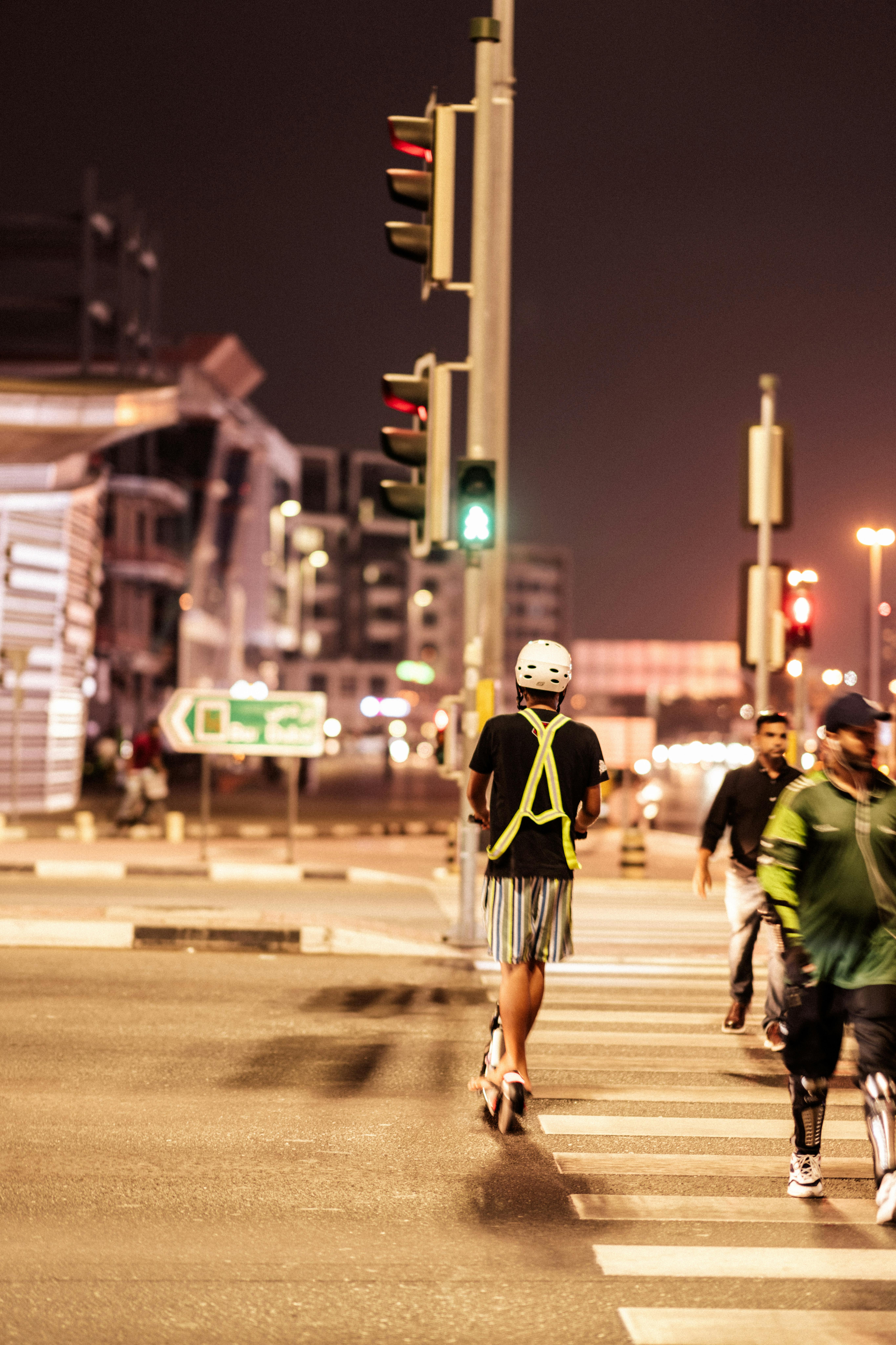 Free A man rides a scooter across a city street at night, showcasing urban nightlife. Stock Photo
