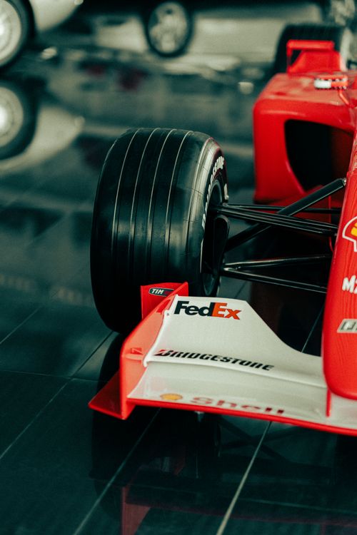 Free Close-up view of a red racing car's wheel and front wing in a polished showroom setting. Stock Photo