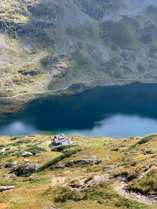 Free Stunning aerial view of a serene mountain lake with a cottage below, surrounded by lush hills. Stock Photo