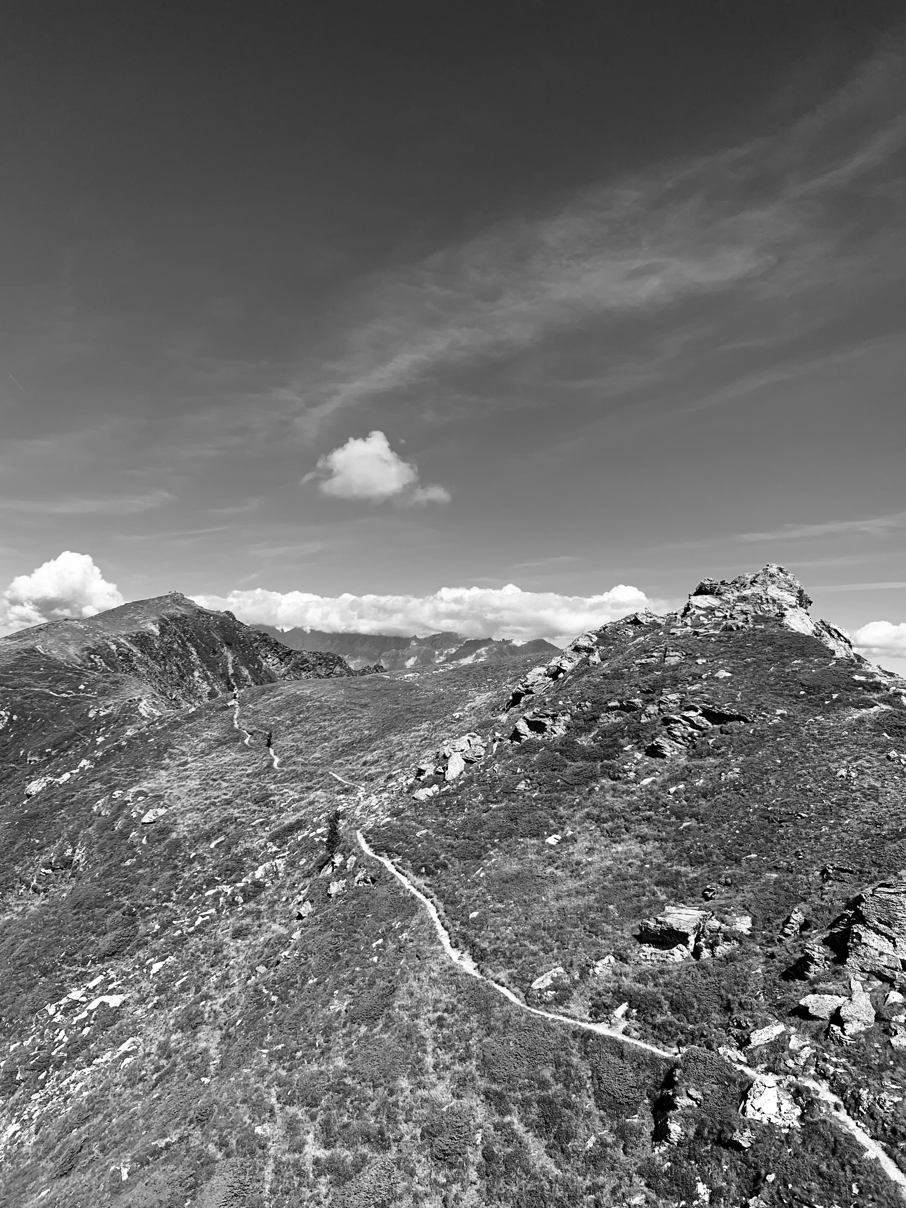 Aerial view of a rocky mountain path under a dramatic sky in black and white.