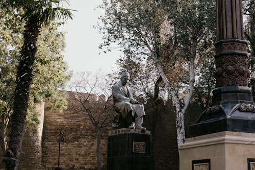 A statue of a man sitting on a bench next to a tree