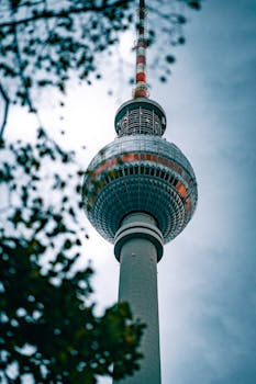 Low-angle shot of the iconic Fernsehturm tower in Berlin, showcasing architectural beauty against a cloudy sky.