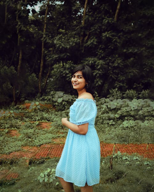 Smiling Woman in Blue Dress Standing on Grass in Park