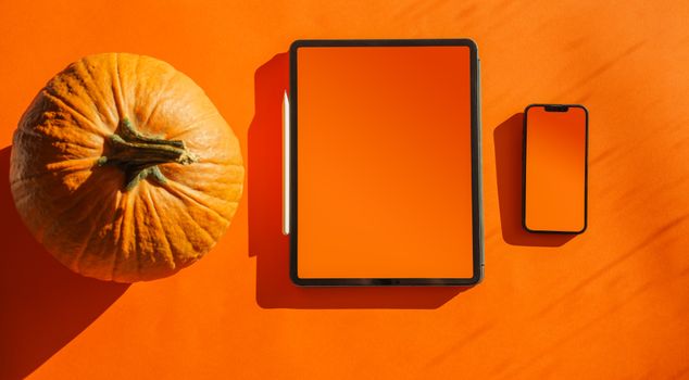 Minimalist autumn-themed mockup with tablet, smartphone, stylus, and pumpkin on orange background.