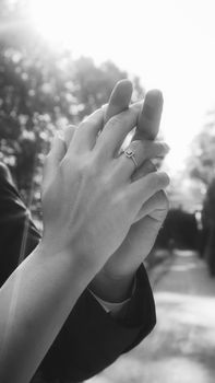 Close-up of intertwined hands displaying an engagement ring outdoors.
