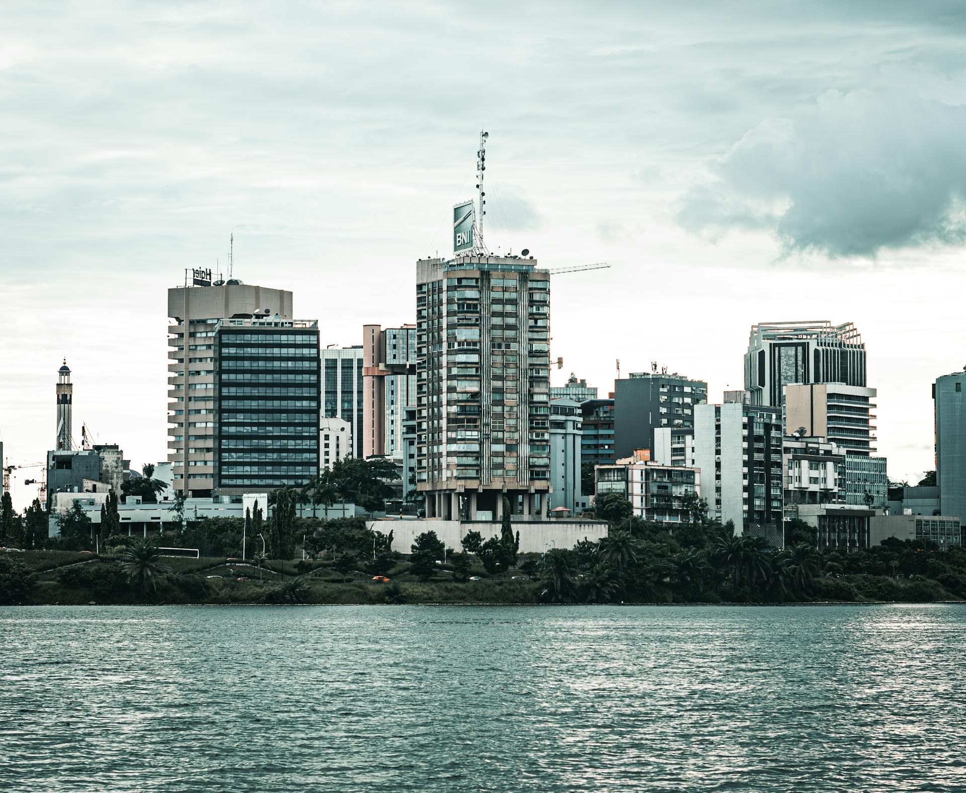 Contemporary cityscape of Abidjan featuring high-rise buildings by the waterfront under overcast skies.