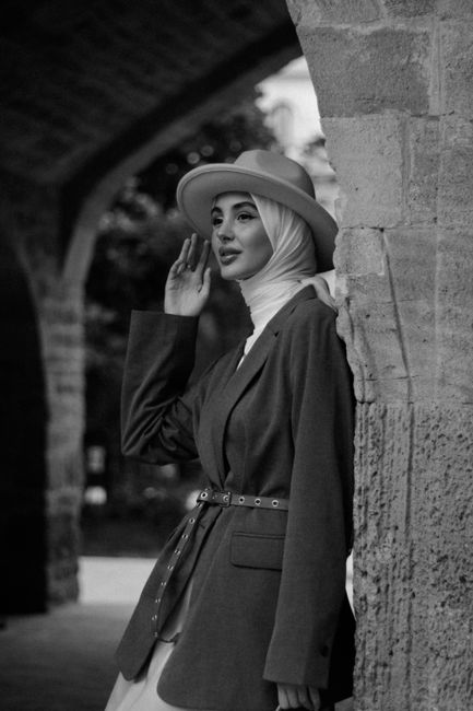 Elegant woman wearing a fedora and hijab, posing in a classic urban environment.