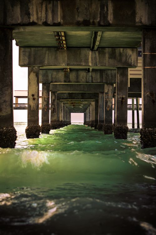Free A mesmerizing perspective under a pier in Clearwater, Florida, with green ocean waves and strong architectural lines. Stock Photo
