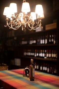 A colorful wine bottle display set under a vintage chandelier with soft lighting, perfect for interior design inspiration.