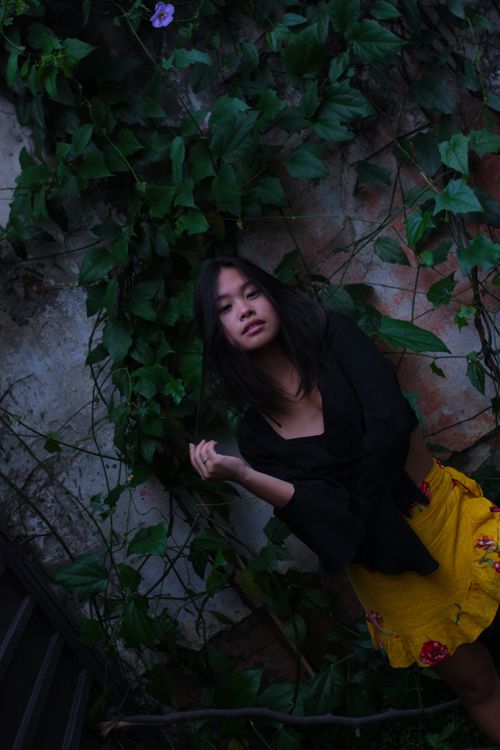 Free Fashionable young woman posing outdoors against a lush ivy-covered wall, exuding style and confidence. Stock Photo