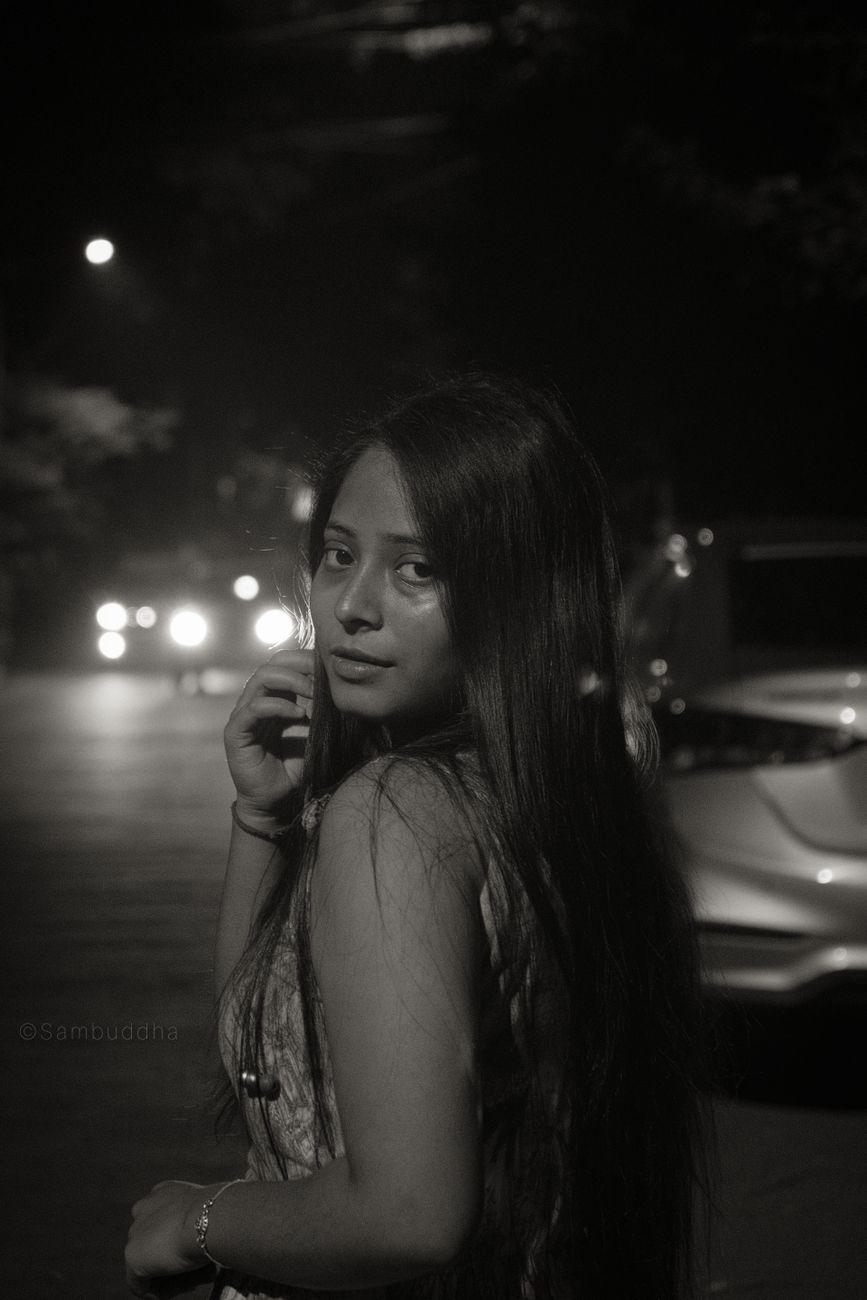 A captivating black and white portrait of a young woman at night, exhibiting mystery and elegance.
