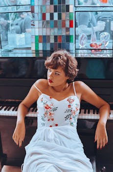 A stylish female model in a floral dress posing elegantly by a piano, exuding grace and sophistication.