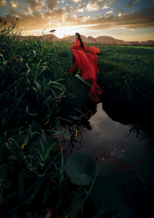 Woman in a Red Dress Posing on a Field at Sunset