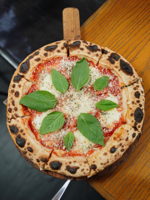 Free Delicious wood-fired Margherita pizza topped with fresh basil leaves, ready to enjoy. Stock Photo