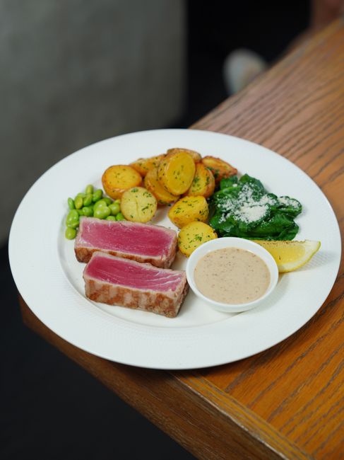 Thinly sliced eye of round steak fanned out on a wooden board, showing a deep brown crust and pink medium-rare center, with a pat of herb butter melting on top.