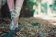 芭蕾舞演员穿着足尖鞋的双脚特写，拍摄于户外铺满树叶的小路上
