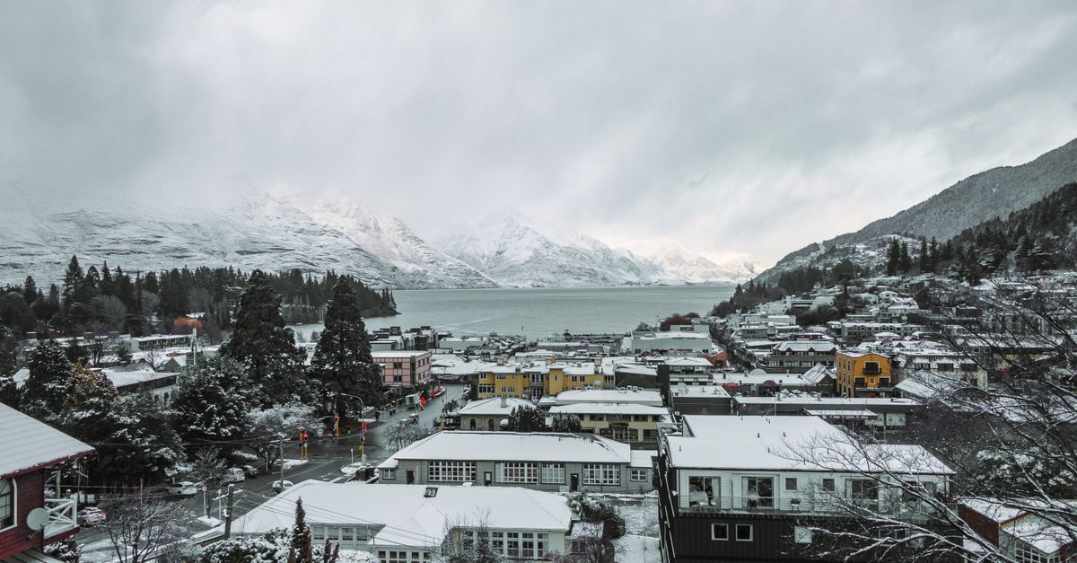 A stunning aerial winter view of Queenstown, New Zealand, showcasing snow-covered buildings and Lake Wakatipu.