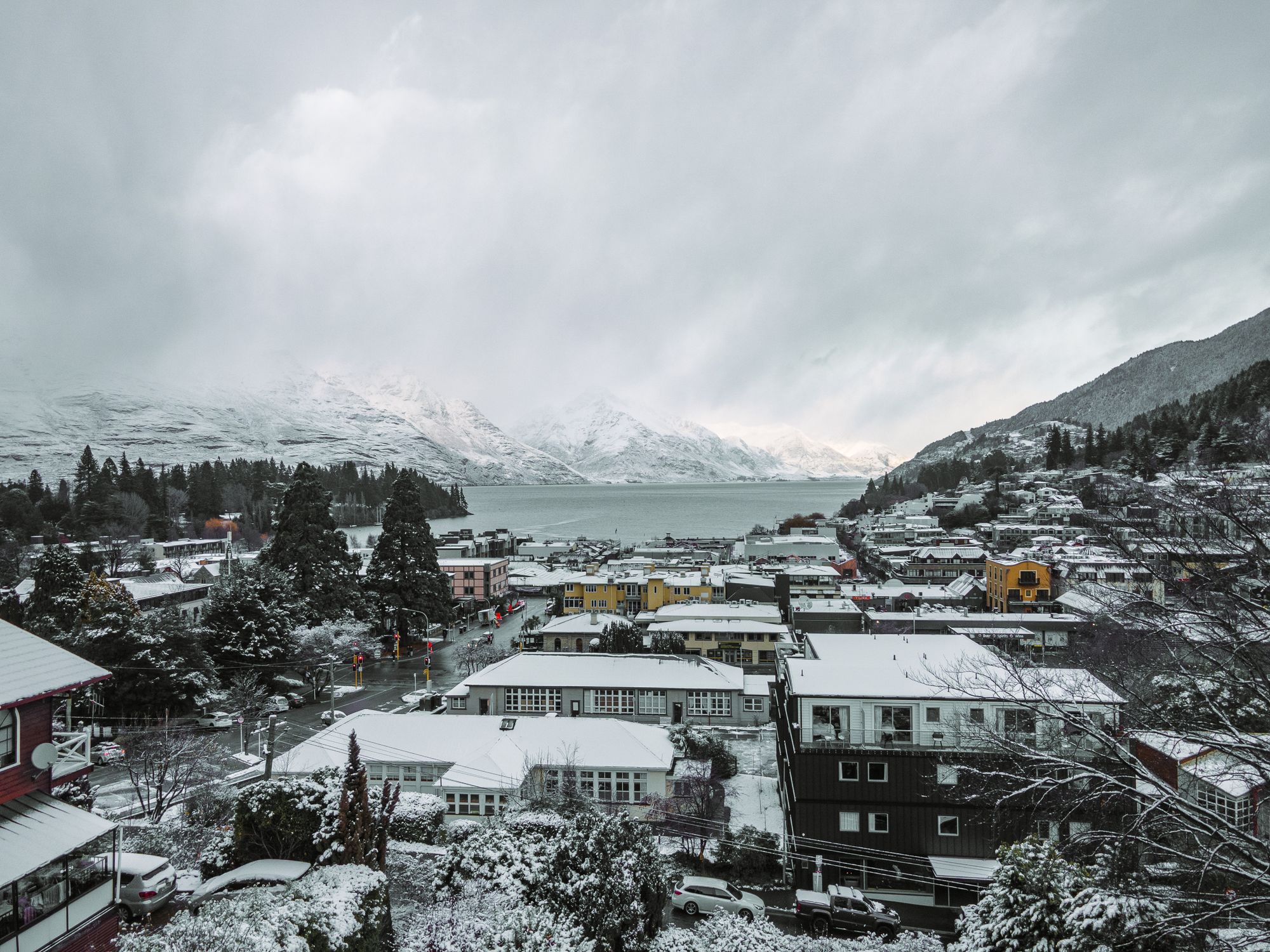 A stunning aerial winter view of Queenstown, New Zealand, showcasing snow-covered buildings and Lake Wakatipu.