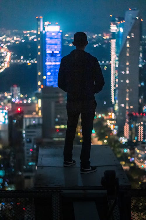 Silhouette of Man Standing on Edge with City Skyscrapers behind