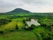 Drone shot showcasing lush green fields, a tranquil lake, and a scenic hill in a rural setting.