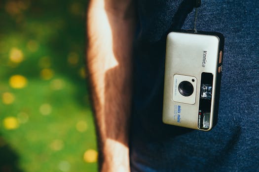 Close-up of a vintage analog camera hanging outdoors on a sunny day, perfect for nostalgia and retro themes.