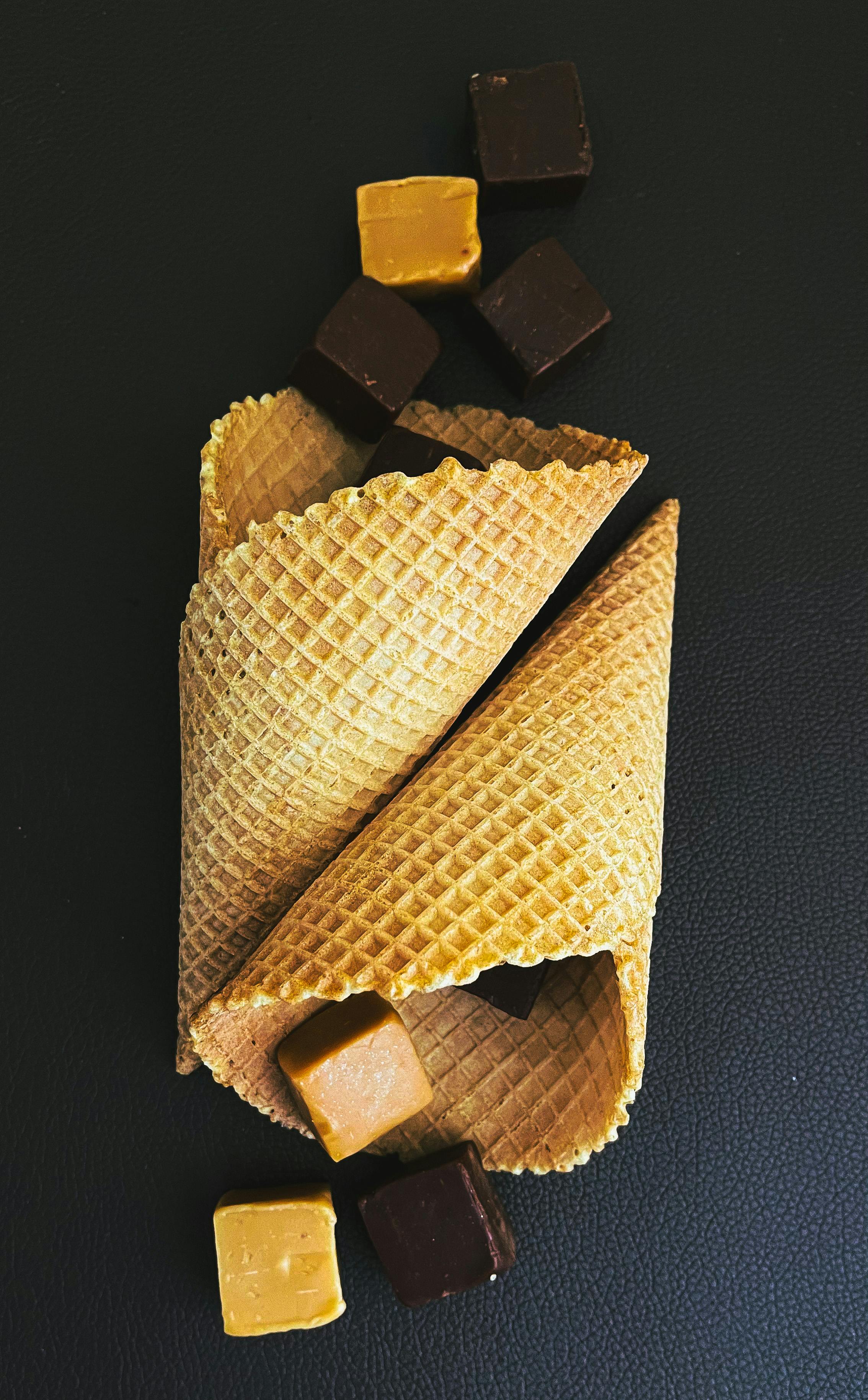 Gourmet waffle cones with chocolate and caramel cubes on black background.