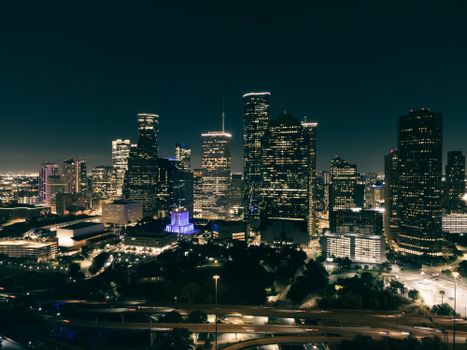 Aerial view of a vibrant city skyline at night with illuminated skyscrapers and roads.
