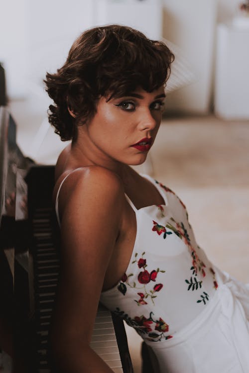 Woman in White and Red Floral Spaghetti Strap Top Leaning on Piano