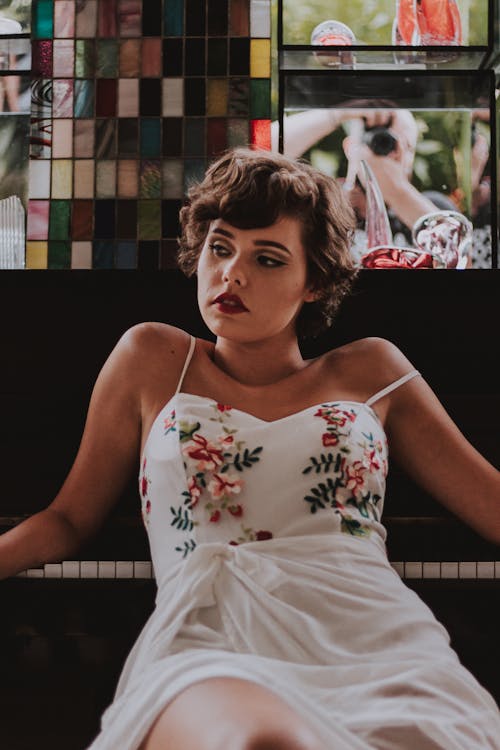 Woman in White Spaghetti Strap Dress Leaning on Piano