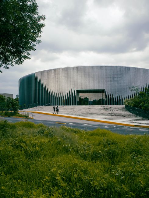 Curved modern building facade in Mexico City with lush greenery and cloudy sky.