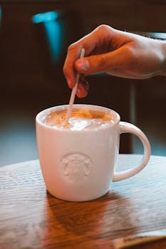 Close-up of a hand stirring coffee in a ceramic mug on a wooden table.