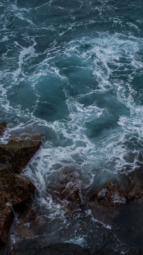 Free Captivating high angle view of ocean waves crashing against rocky shore with vibrant water textures. Stock Photo