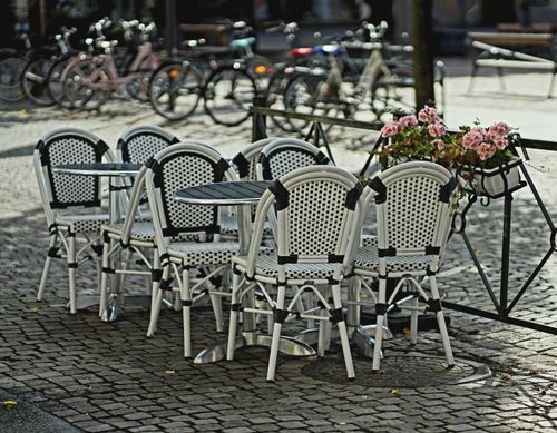 Free Outdoor cafe with white chairs and tables, bicycles in the background, and floral decorations. Stock Photo