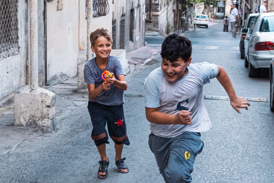 Two boys joyfully run through a lively city street, embodying fun and carefree childhood moments.