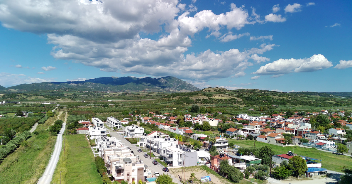 Aerial view of a picturesque town surrounded by lush greenery and mountains under a clear blue sky.