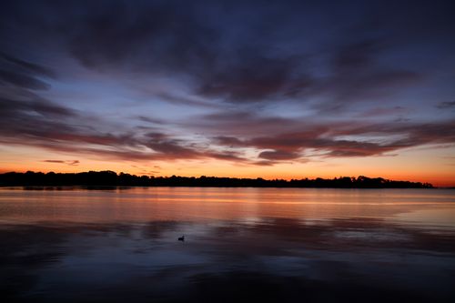 Free A tranquil sunset with vibrant clouds reflected on a calm lake, creating a serene natural scenery. Stock Photo