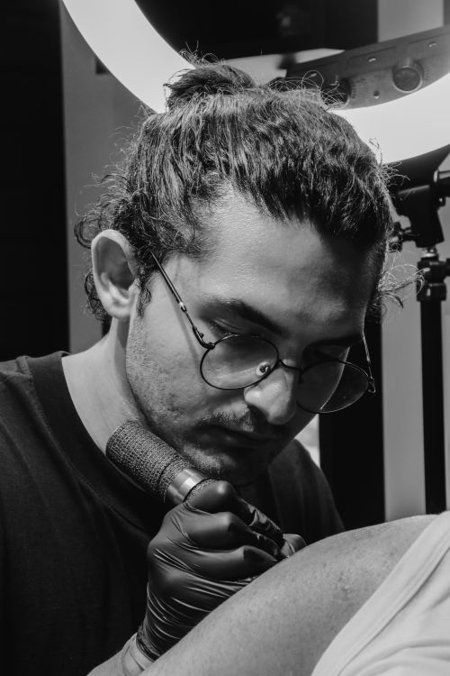 Free Black and white image of a tattoo artist concentrating while tattooing indoors. Stock Photo