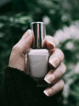 Natural manicure with delicate floral design holds a nail polish bottle.