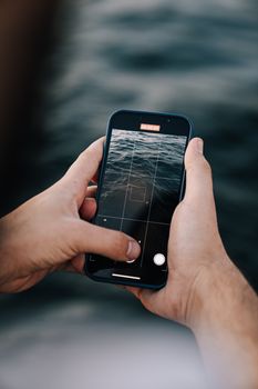 A person uses a smartphone to capture rippling water in a vertical shot outdoors.