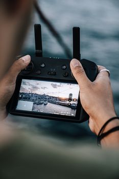 Man operates a drone controller displaying an oceanic view on its screen.