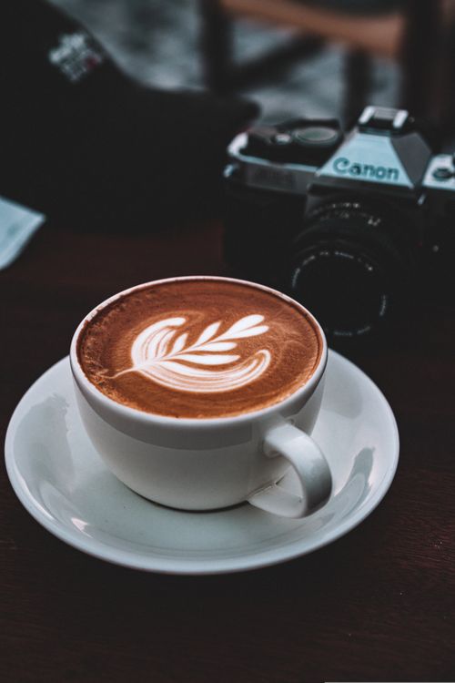 Free Coffee cup with latte art and camera on table in a cozy café atmosphere. Stock Photo