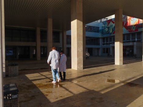 Two doctors in white coats walking through an outdoor hospital courtyard.
