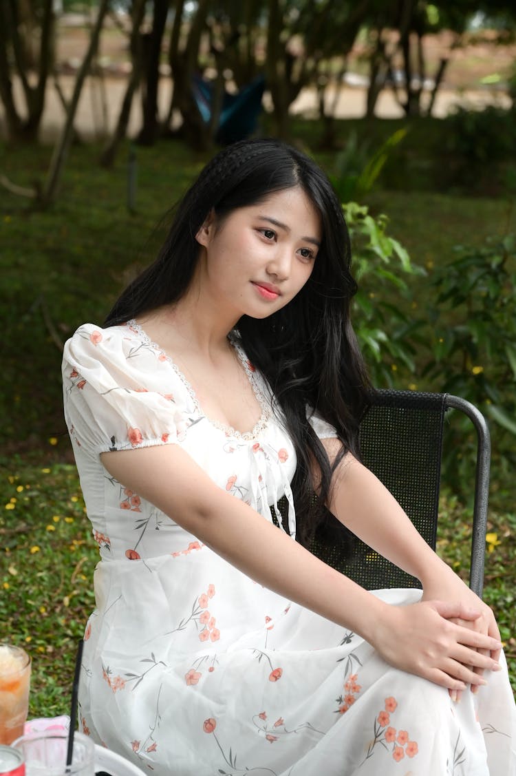 Young Asian Woman In Dress Sitting On Chair In Park