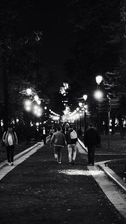 People Walking on Night Road with Street Lamps