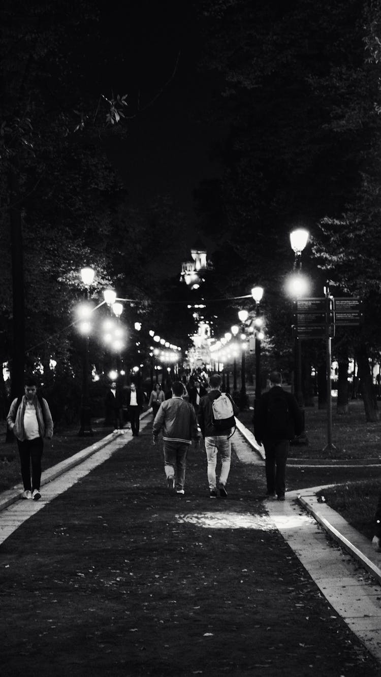 People Walking On Night Road With Street Lamps