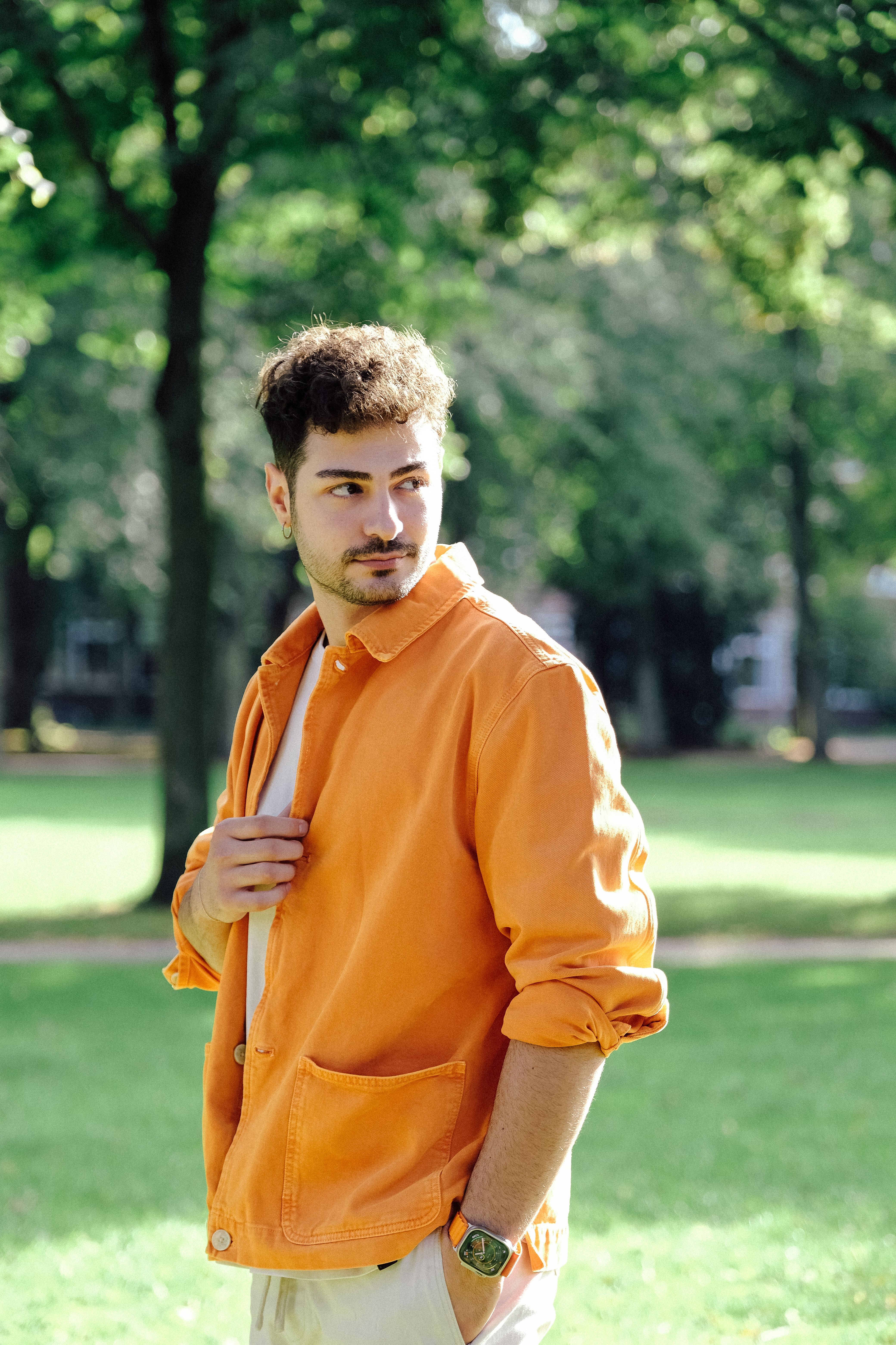 Brunette Man in Orange Overshirt Standing in a Park · Free Stock Photo