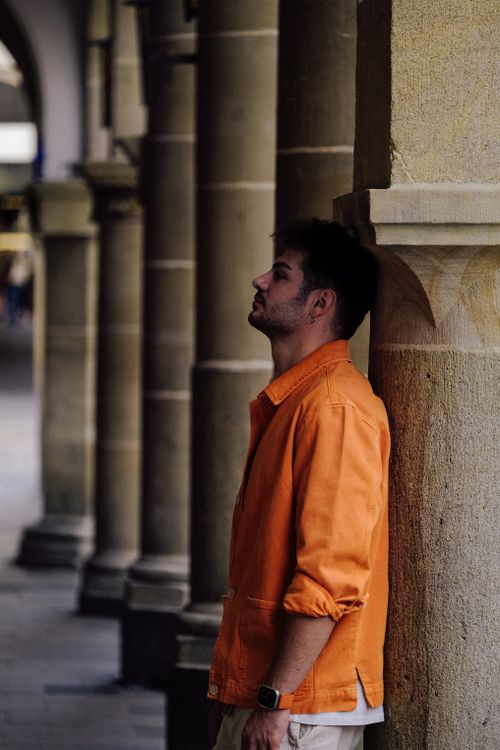 Free A man in an orange shirt stands by ancient columns capturing urban fashion essence. Stock Photo