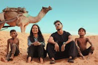 一群朋友坐在沙漠中的沙滩上，与骆驼一起享受着阳光明媚的一天